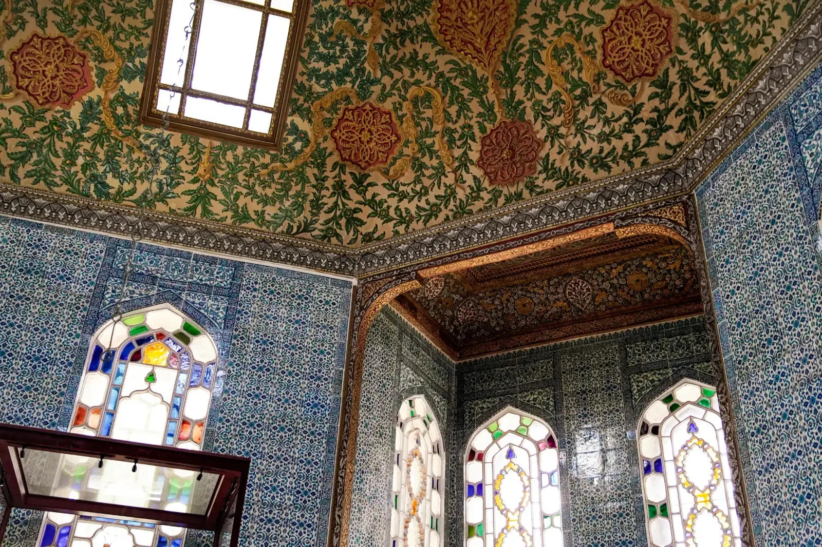 Stained glass and İznik tiles beneath a painted vault in a Fourth Courtyard pavilion.