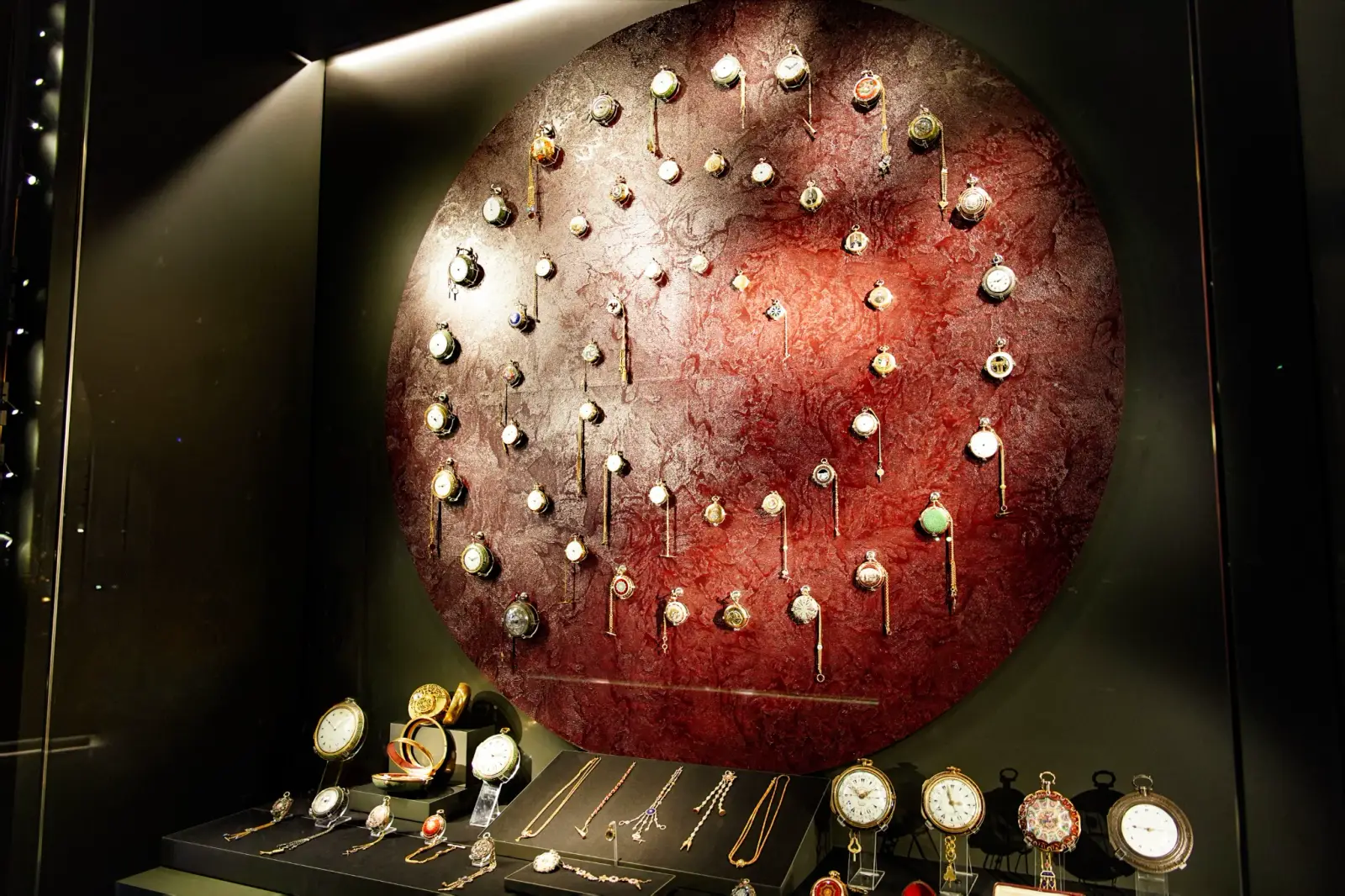 Pocket watches and chains arranged across a red disc in the Clock Museum.