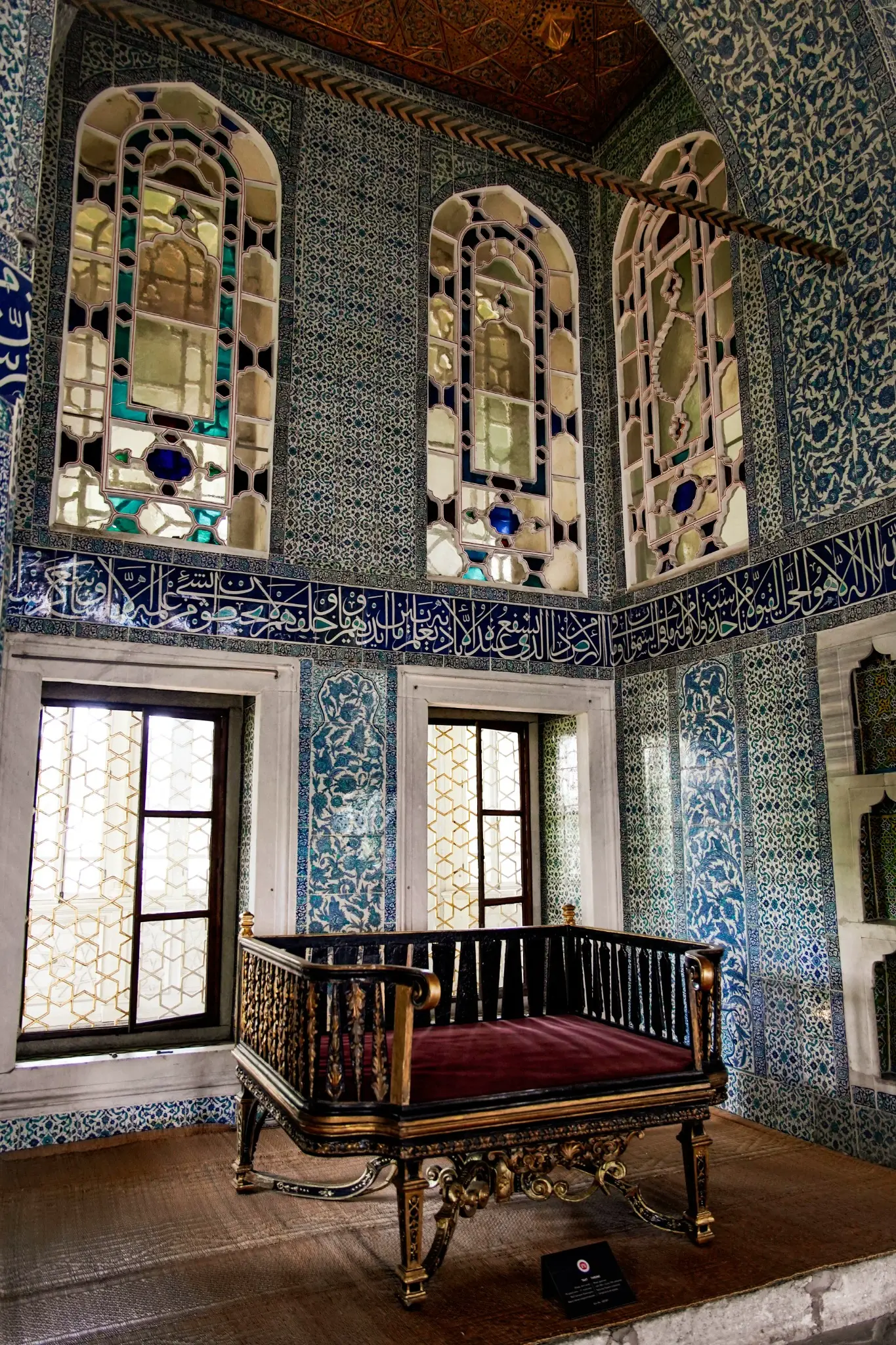 A tiled Harem chamber, stained glass above a low wooden seat.