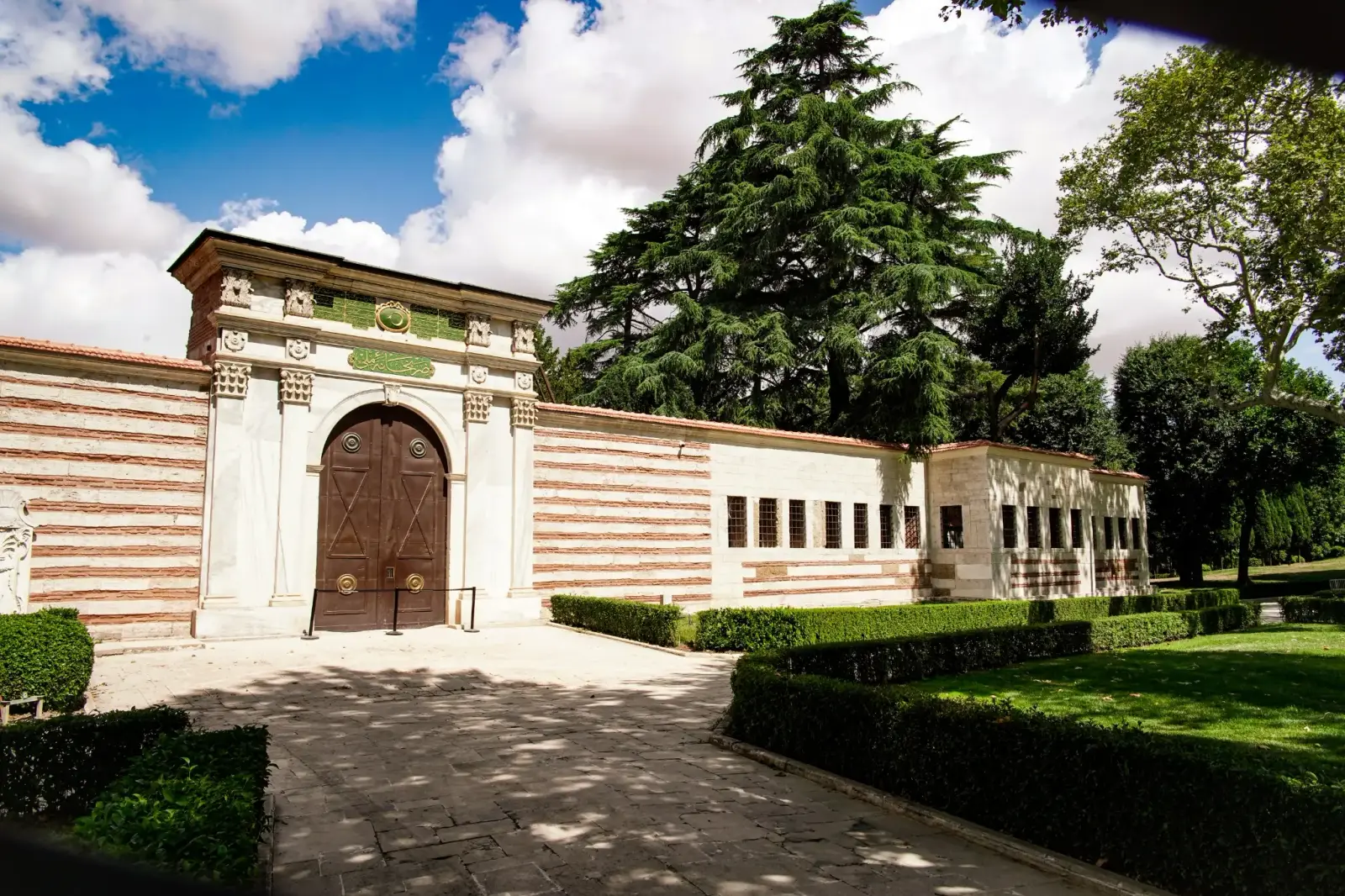 The gate of the Imperial Mint, striped ashlar walls beneath a cedar in the First Courtyard.