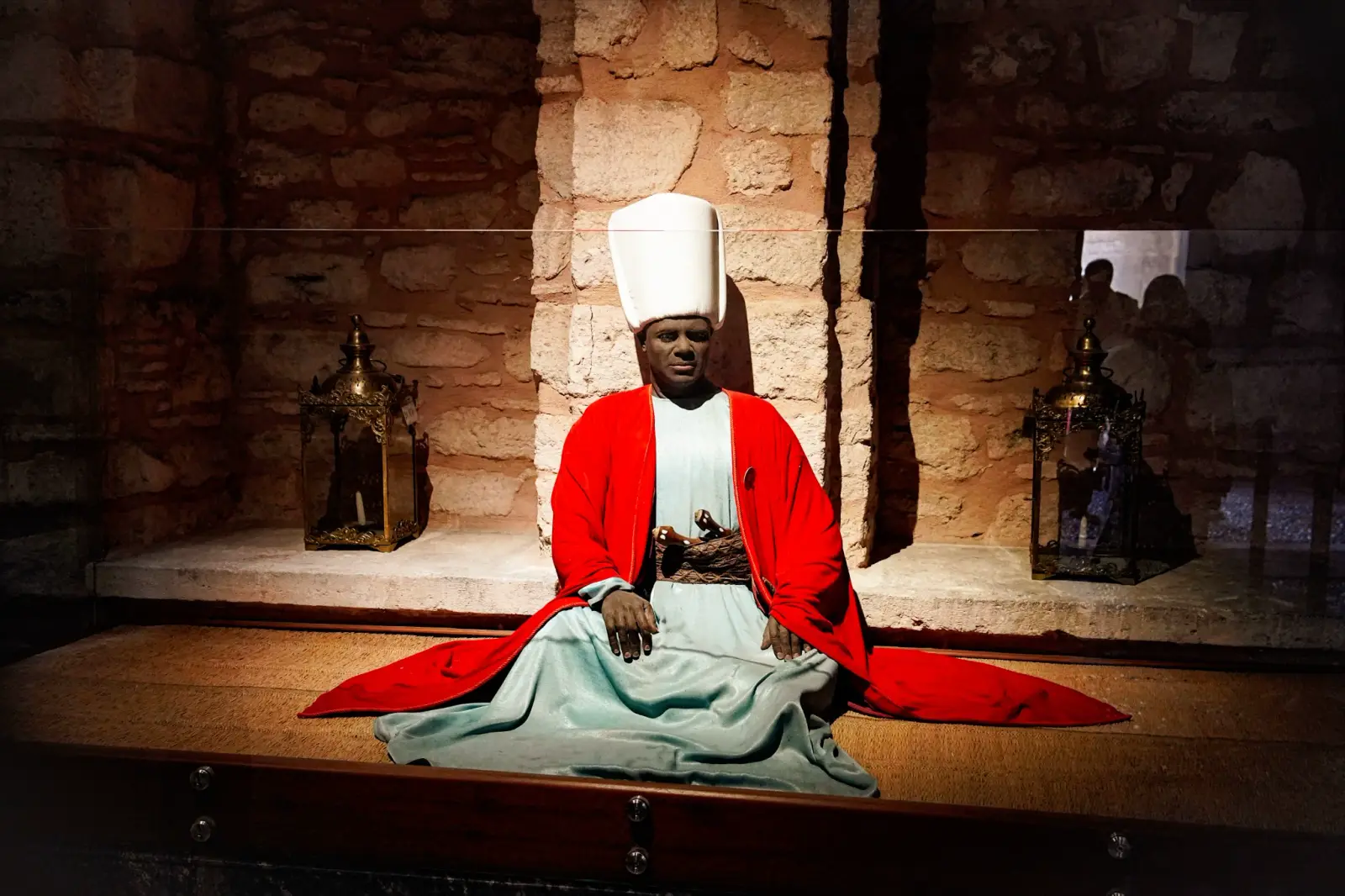 A costumed figure of a Black Eunuch of the Harem, in a red robe and tall white cap, in the eunuchs' quarters.