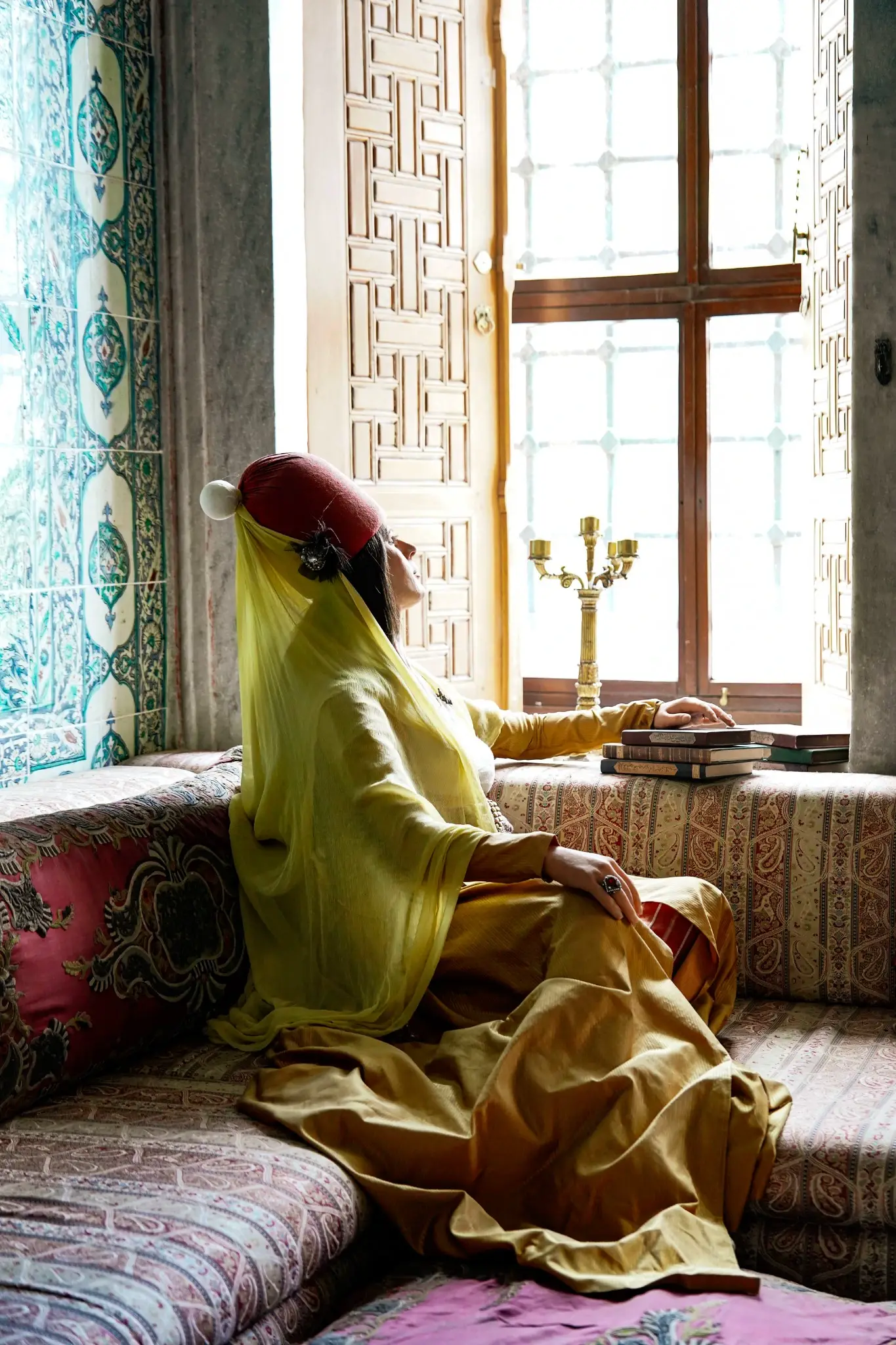 A costumed figure reading at a Harem window, calligraphic panels on the wall behind.