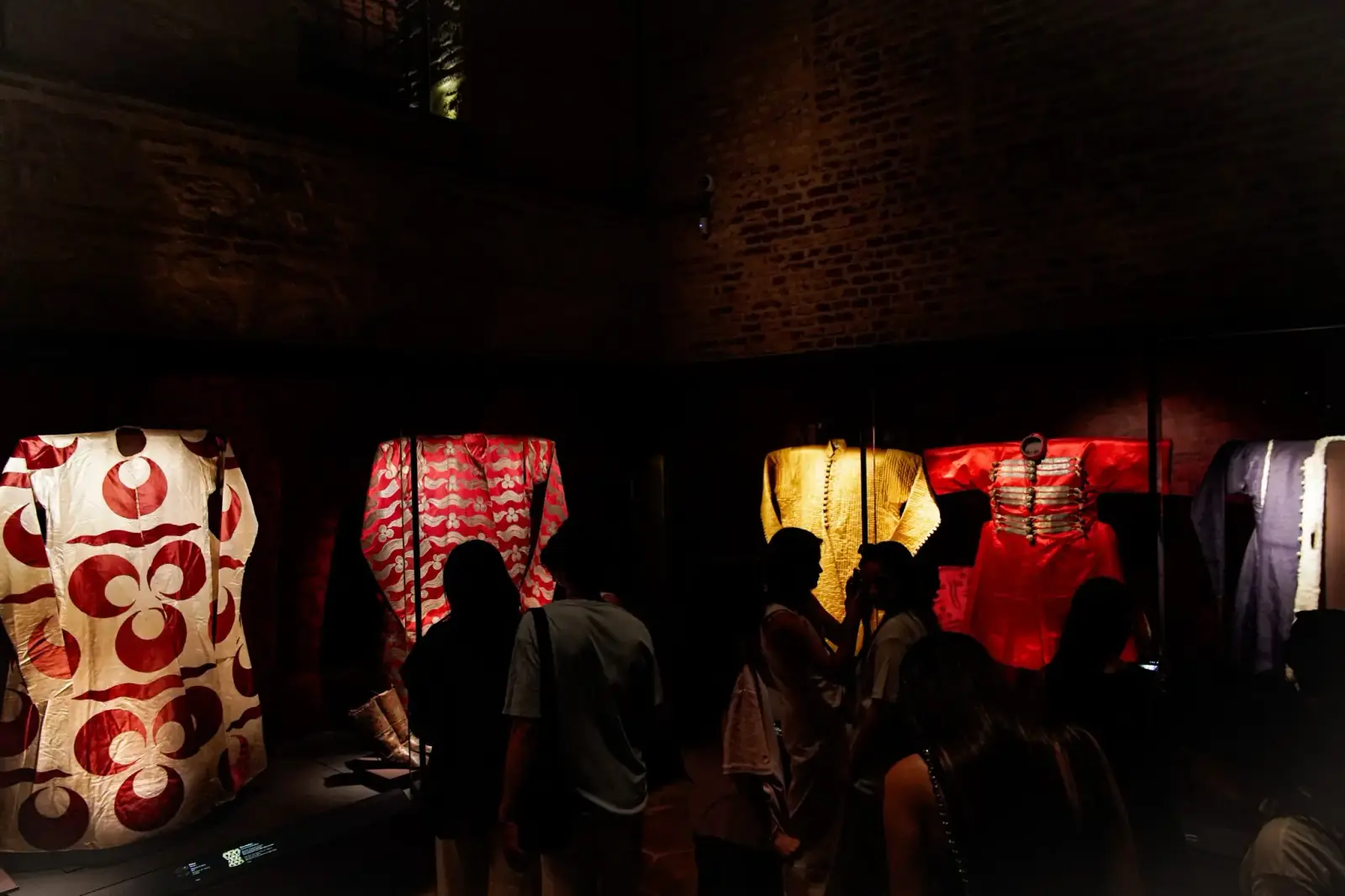 Imperial kaftans lit in a darkened gallery, visitors moving between the cases.