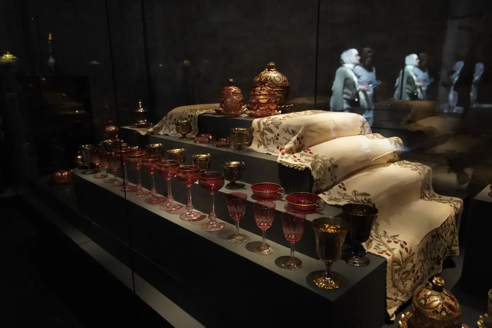 Ruby and gilt glassware from the palace, ranged along a case with embroidered cloths.