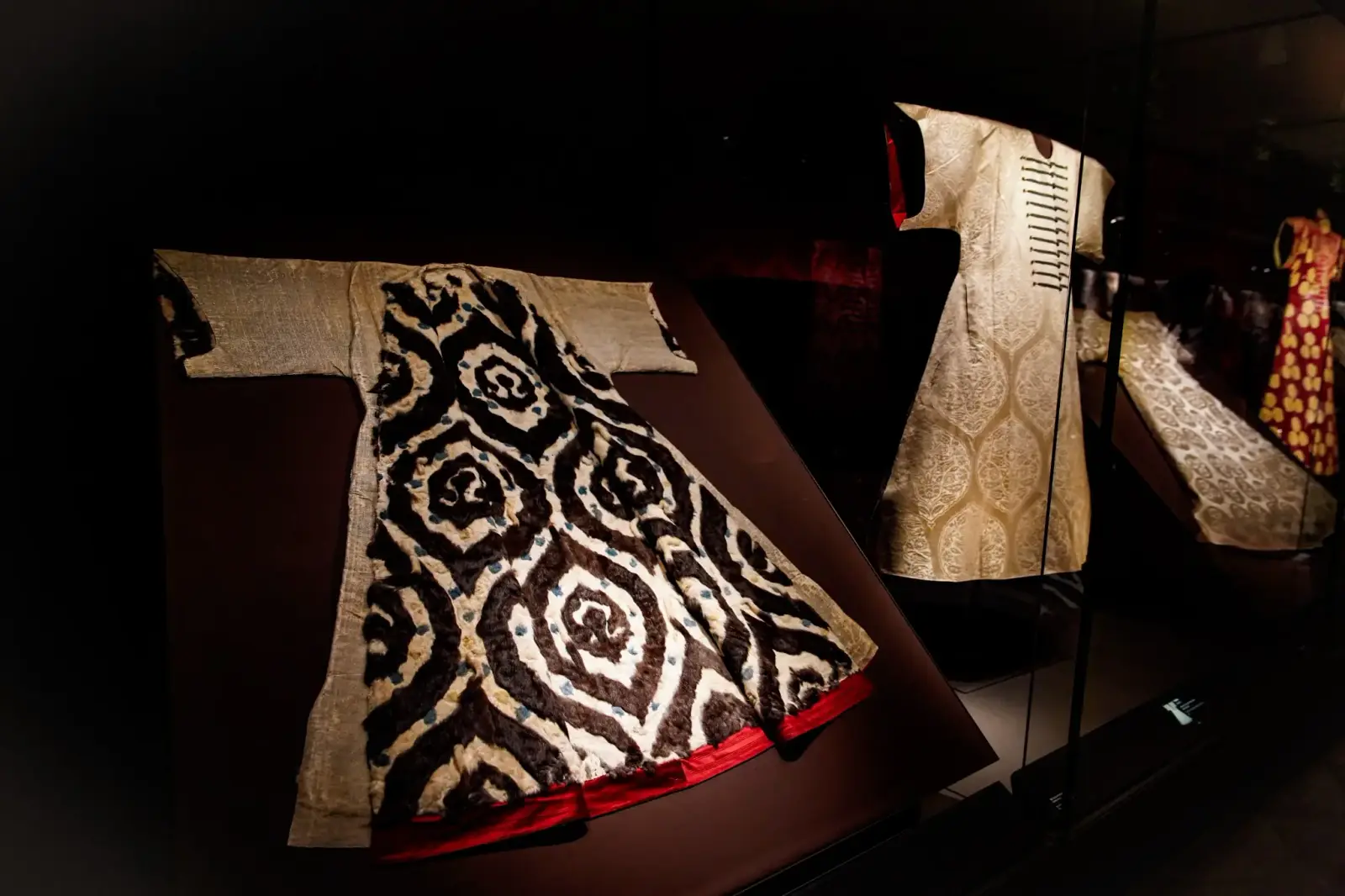 A kaftan patterned in black and white beside a plainer robe in the costume gallery.